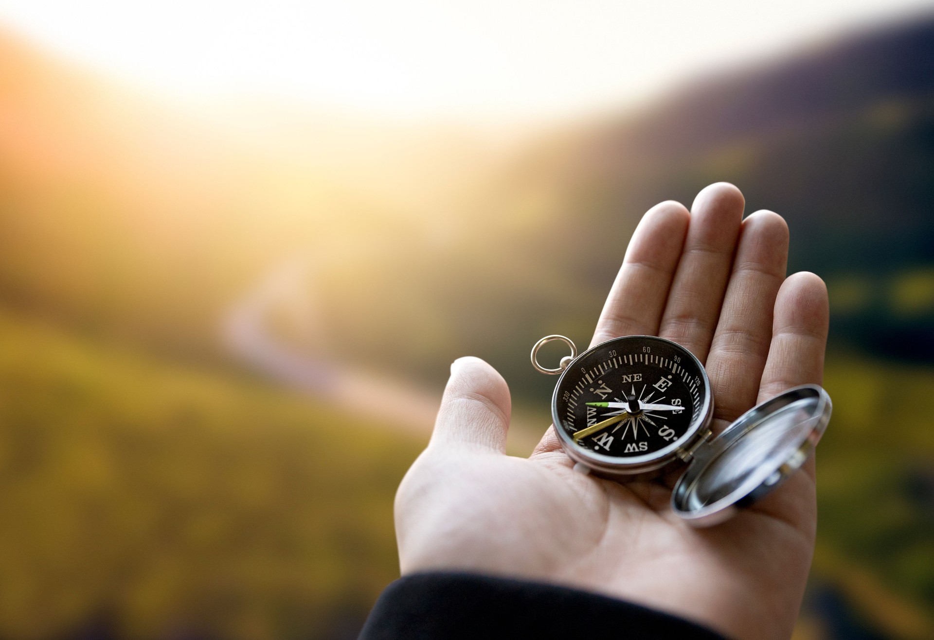 Traveler explorer man holding compass in a hand in mountains at sunrise, point of view.
